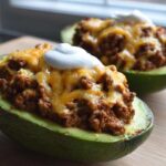 Close-up of Keto Taco Stuffed Avocados filled with seasoned ground meat, melted cheddar cheese, and a dollop of sour cream.