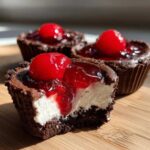 A bite taken out of a No-Bake Chocolate Cherry Cheesecake Cup showing the layers of chocolate crust, white filling, and cherry topping.