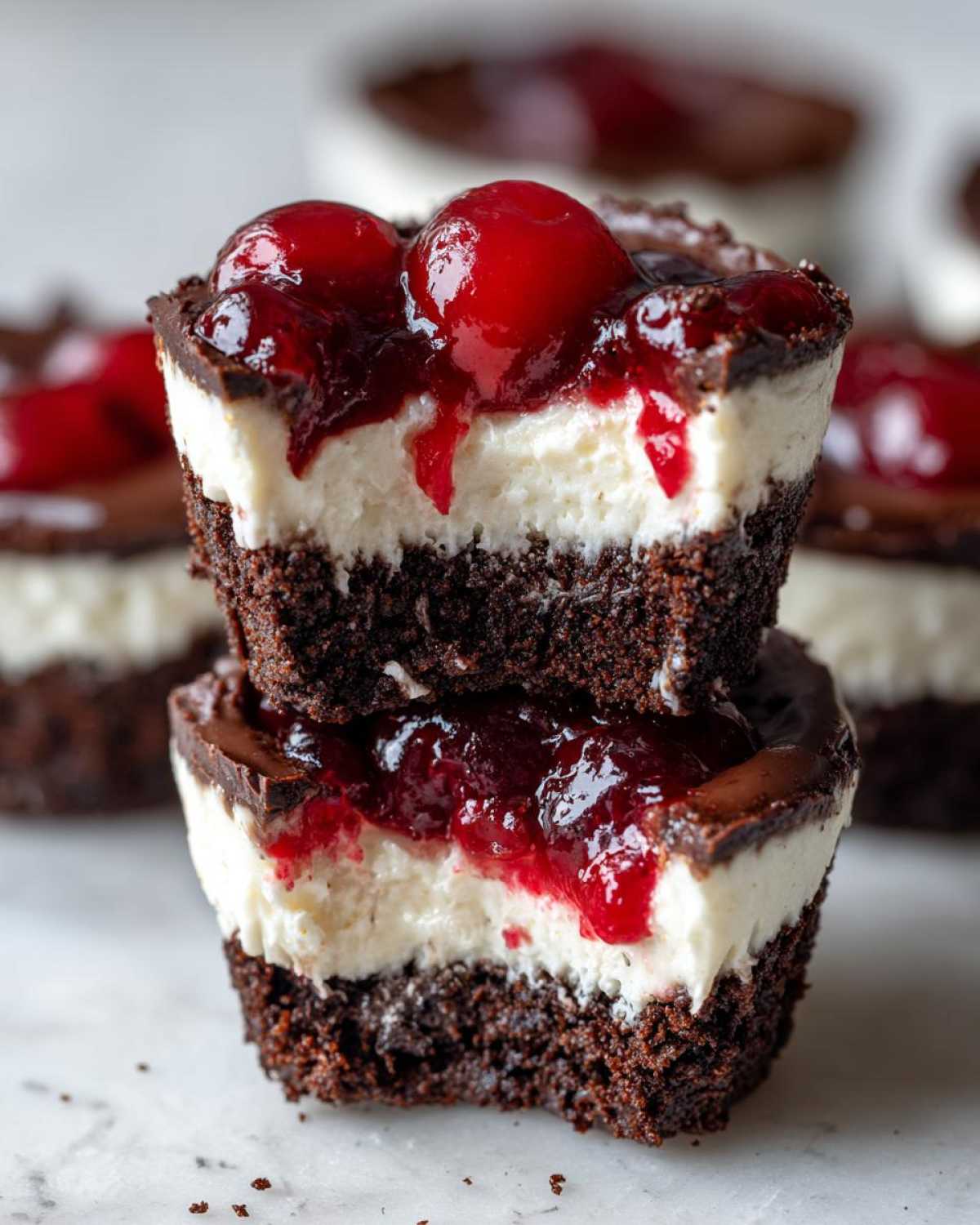Two stacked No-Bake Chocolate Cherry Cheesecake Cups showing layers of chocolate crust, cream cheese filling, and cherry topping.