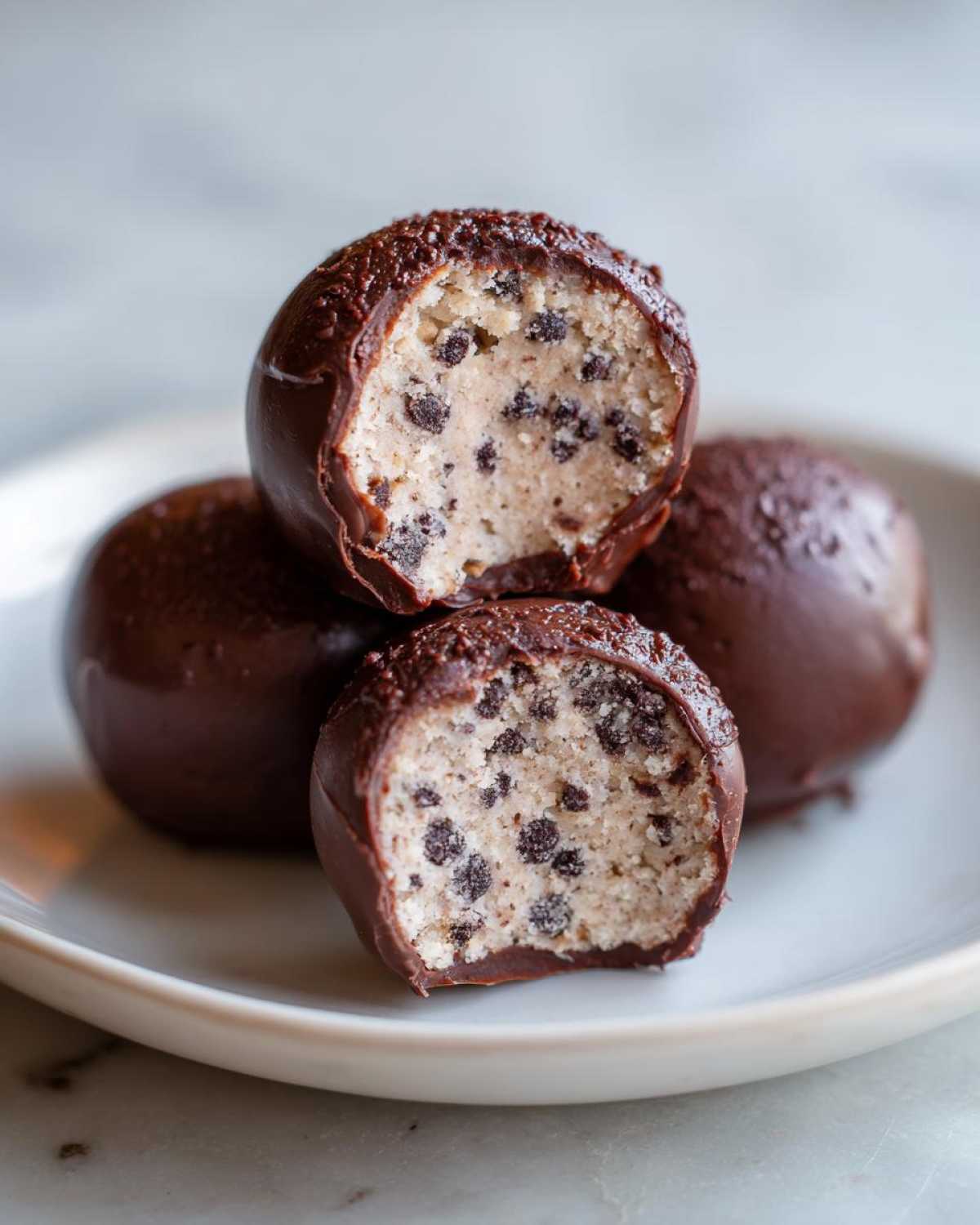 Close-up of No-Bake Chocolate Chip Cookie Dough Truffles, one cut open showing the dough interior.