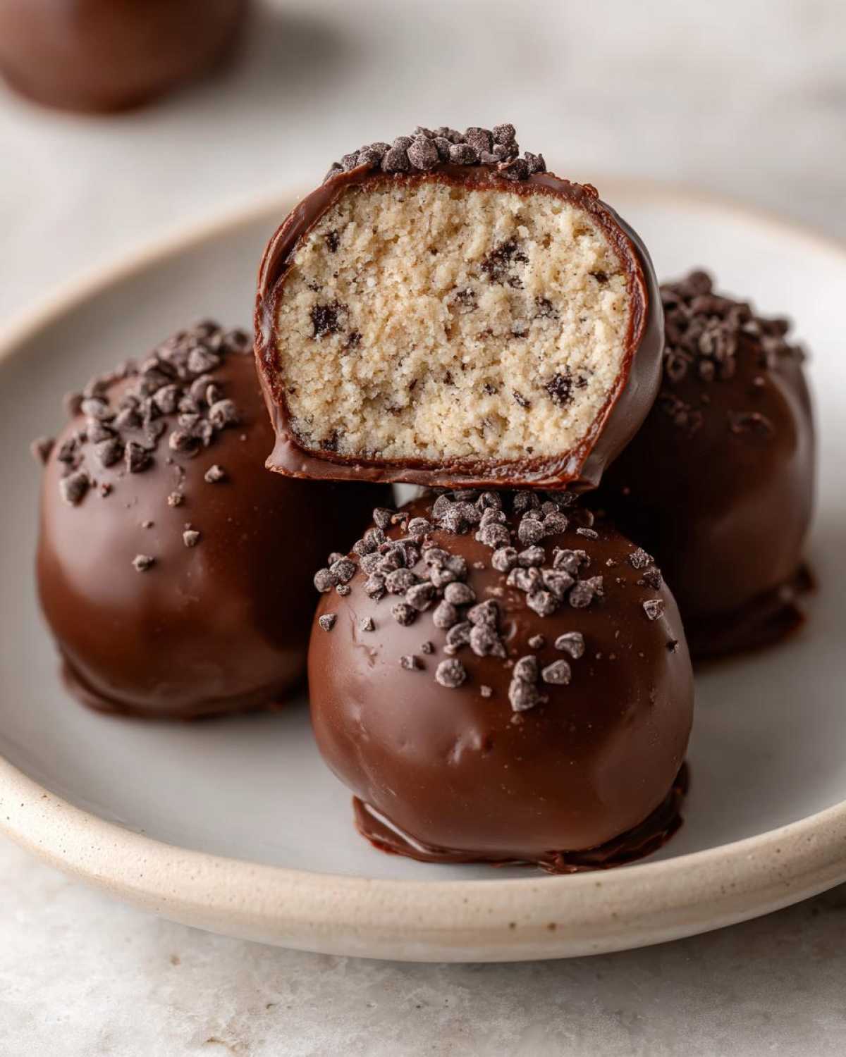 Close-up of chocolate-dipped No-Bake Chocolate Chip Cookie Dough Truffles, one cut open to show the dough interior.