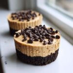 Close-up of a No-Bake Chocolate Peanut Butter Cheesecake Cup with a dark crust and peanut butter filling topped generously with chocolate chips.