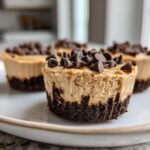 A close-up view of a No-Bake Chocolate Peanut Butter Cheesecake Cup with a dark crust and peanut butter filling topped with chocolate chips.
