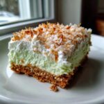 A square slice of No-Bake Coconut Lime Bars featuring a graham cracker crust, light green filling, and toasted coconut topping.
