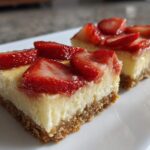 Two squares of No-Bake Strawberry Lemon Cheesecake Bars with thick graham cracker crust and fresh strawberry topping.