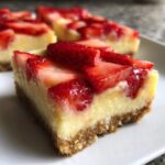 A close-up of a No-Bake Strawberry Lemon Cheesecake Bars slice showing the graham cracker crust and strawberry topping.