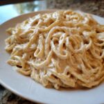 Close-up of fettuccine pasta generously coated in rich Vegan Creamy Cashew Alfredo Sauce on a white plate.