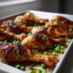 Close-up of glossy, roasted Sheet Pan Lemon Garlic Butter Chicken Legs with bright green peas.
