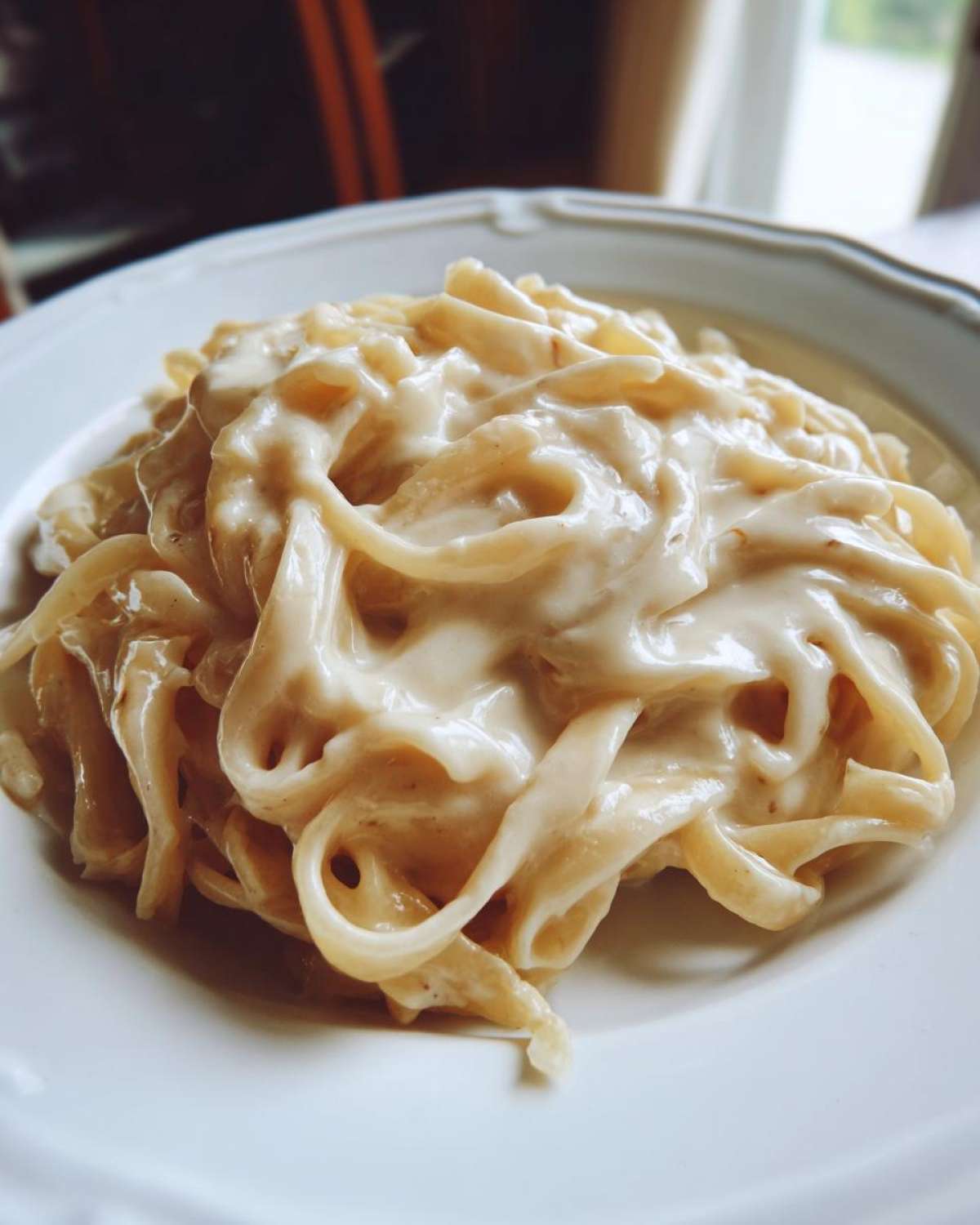 Close-up of fettuccine pasta generously coated in rich Vegan Creamy Cashew Alfredo Sauce on a white plate.