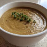 A close-up of a white bowl filled with rich Vegan Creamy Mushroom Soup with Thyme garnish.