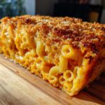 A thick slice of Cheesy Baked Mac and Cheese with Crispy Top showing creamy interior and browned breadcrumbs.