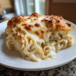 A generous serving of Cheesy Chicken Alfredo Bake with creamy sauce and a bubbly, browned cheese topping on a white plate.