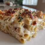 Close-up of a baked serving of Cheesy Chicken Alfredo Bake with Mozzarella, showing browned cheese and pasta tubes.