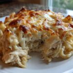 A close-up serving of Cheesy Chicken Alfredo Bake showing shredded chicken, pasta, and a bubbly, browned cheese topping.