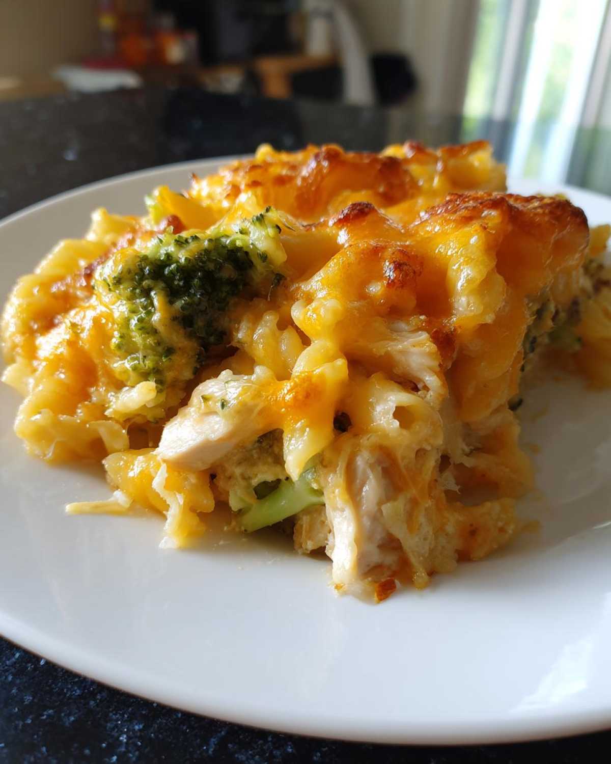 A close-up serving of Cheesy Chicken and Broccoli Pasta Bake with melted, golden-brown cheese topping.