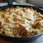 A close-up of a Cheesy Chicken and Rice Skillet with Cream Sauce, topped with melted cheese and chunks of chicken.