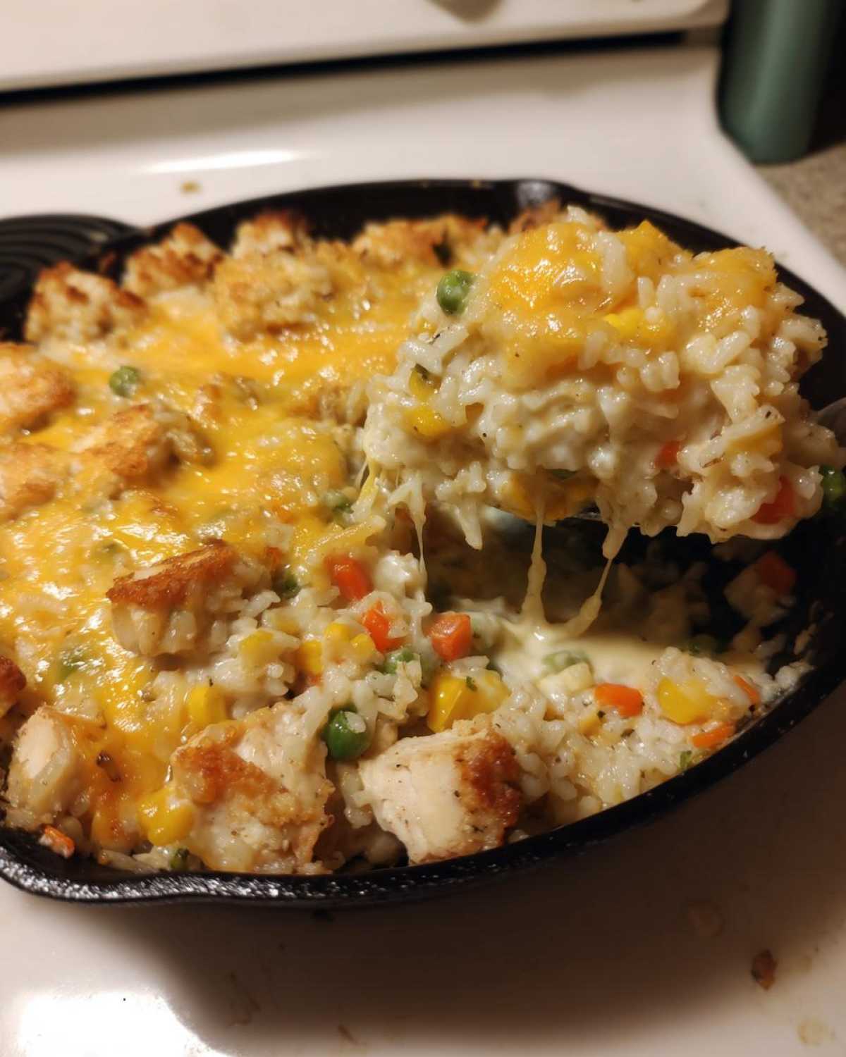 A spoonful of Cheesy Chicken and Rice Skillet with Cream Sauce showing melted cheese pulling away from the dish in a cast iron pan.