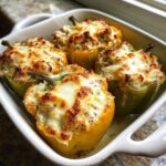 Four baked Cheesy Chicken Stuffed Bell Peppers with melted, browned cheese topping in a white baking dish.