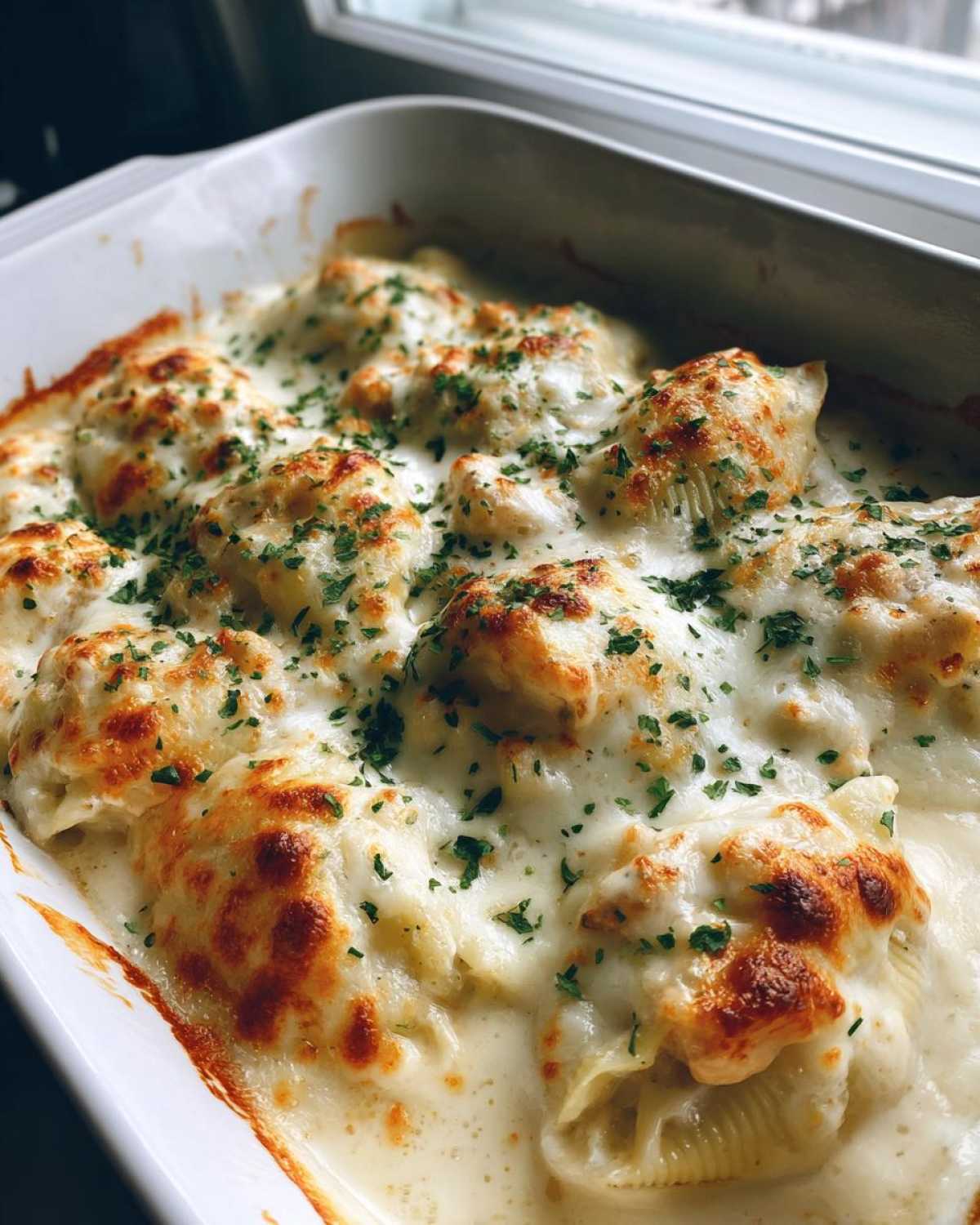 Close-up of baked Cheesy Chicken Stuffed Pasta shells covered in melted, browned cheese and cream sauce, sprinkled with parsley.
