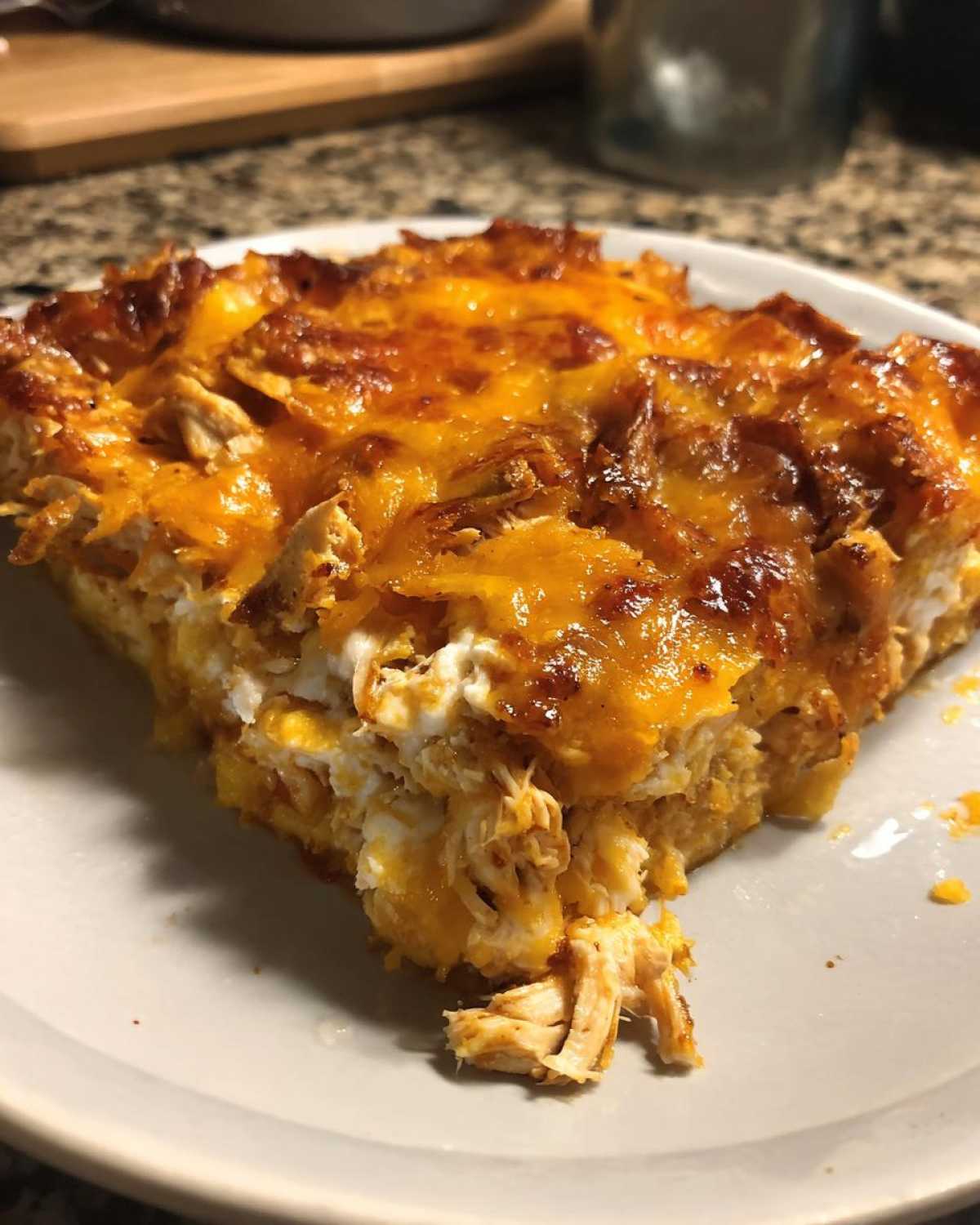 A close-up of a serving of Cheesy Chicken Tortilla Bake, showing shredded chicken and a thick, melted, bubbly cheddar cheese topping.