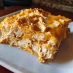 Close-up of a hearty slice of Cheesy Chicken Tortilla Bake showing shredded chicken layered under melted orange and white cheese.
