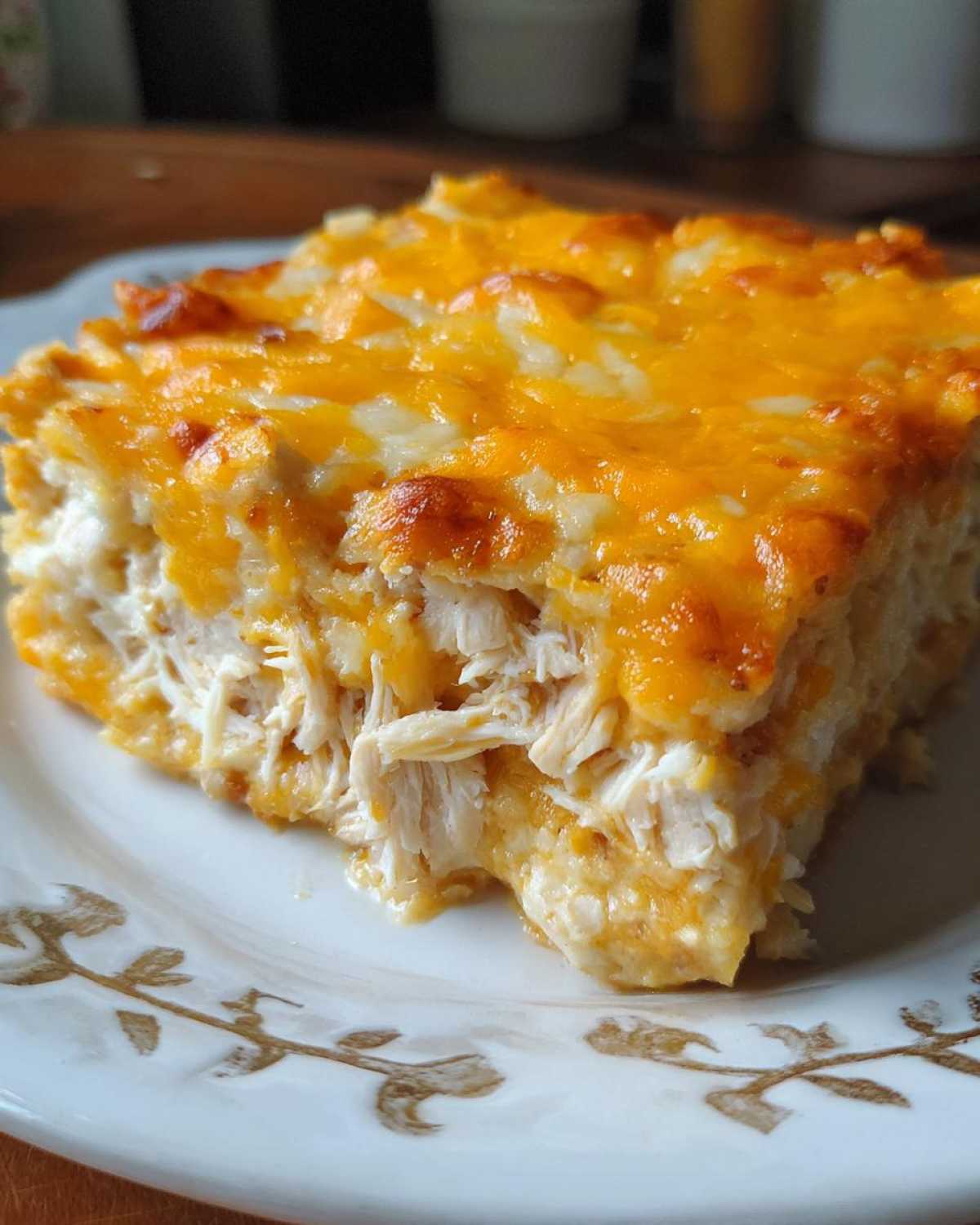 Close-up of a square serving of Cheesy Chicken Tortilla Bake, showing shredded chicken under a thick layer of melted orange and white cheese.