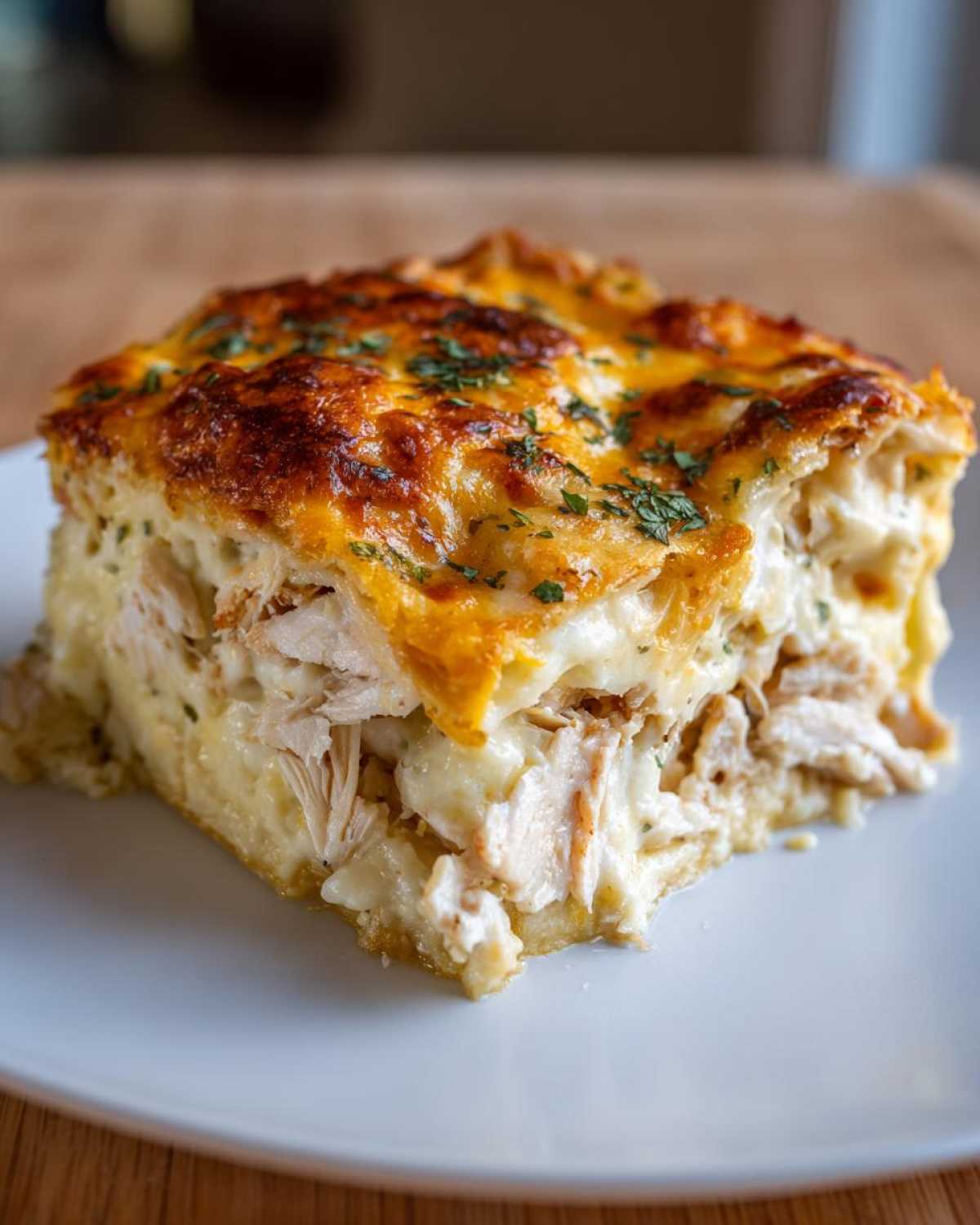 A square serving of Cheesy Chicken Tortilla Bake showing layers of shredded chicken and creamy sauce under a melted, golden-brown cheese crust.