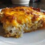 A close-up serving of Cheesy Chicken Tortilla Bake showing shredded chicken and a thick, bubbly layer of melted cheddar cheese.