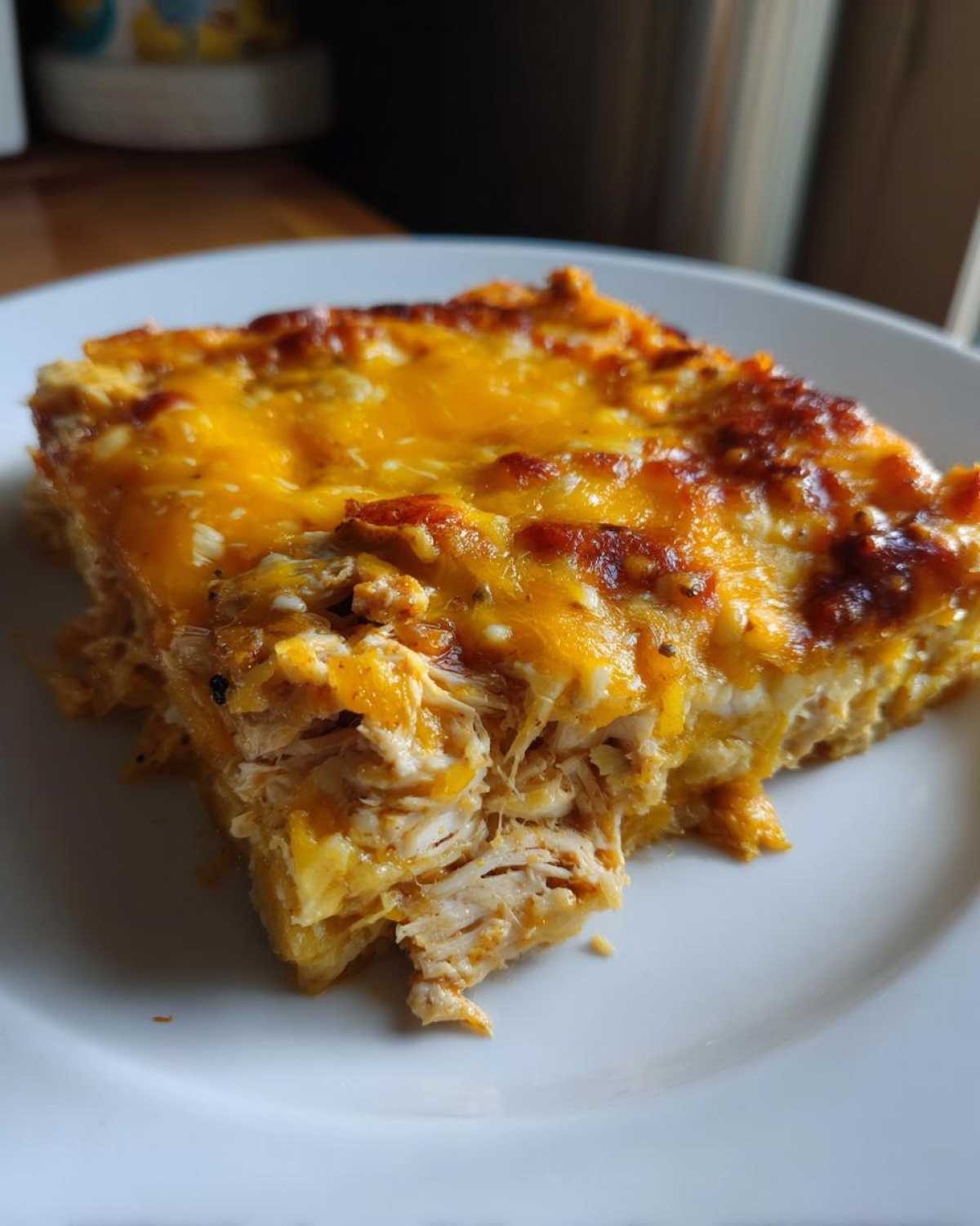 Close-up of a serving of Cheesy Chicken Tortilla Bake showing shredded chicken and a thick layer of melted, browned cheddar cheese.
