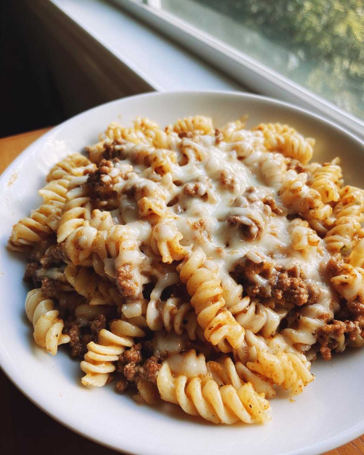 Close-up of a bowl of Cheesy Ground Beef Pasta Skillet featuring rotini pasta, seasoned ground beef, and melted white cheese.