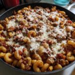 A close-up view of Cheesy Ground Beef Pasta Skillet cooked in a black pan, topped with melted mozzarella cheese.