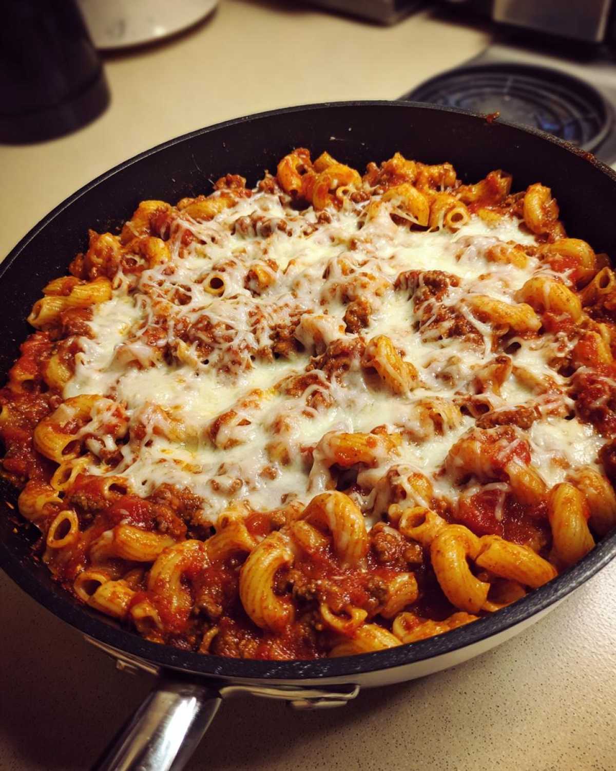 Close-up of Cheesy Ground Beef Pasta Skillet topped with melted mozzarella cheese in a black skillet.