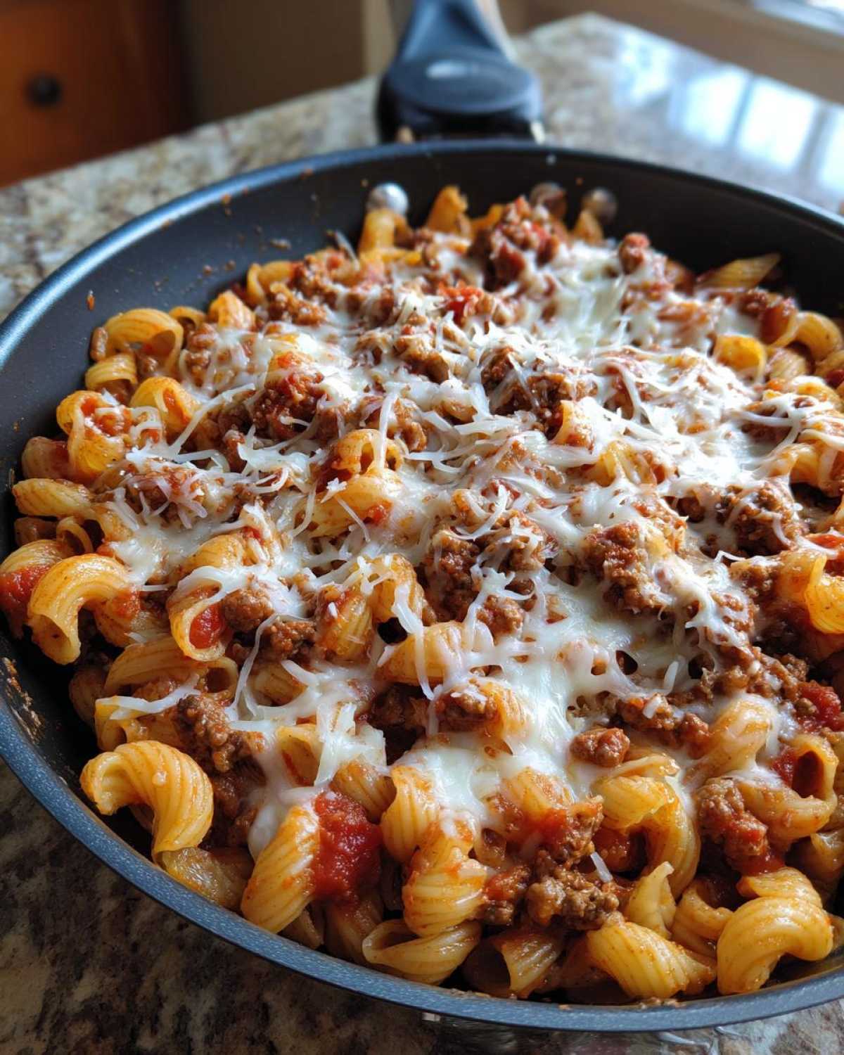 A close-up view of Cheesy Ground Beef Pasta Skillet in a black pan, topped with melted mozzarella cheese.