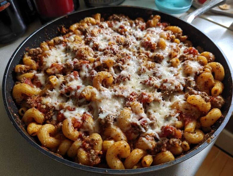 A close-up view of Cheesy Ground Beef Pasta Skillet cooked in a black pan, topped with melted mozzarella cheese.