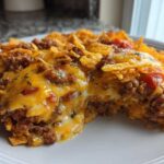 A serving of Cheesy Ground Beef Queso Bake Comfort Dish, showing melted cheese, seasoned ground beef, and crushed tortilla chips.