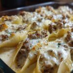 Close-up of baked Cheesy Ground Beef Stuffed Shells with melted mozzarella and cream sauce in a glass dish.