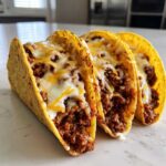 Three hard-shell tacos filled with seasoned ground beef and topped with melted white and yellow cheese, showcasing the Cheesy Ground Beef Tacos with Creamy Filling.