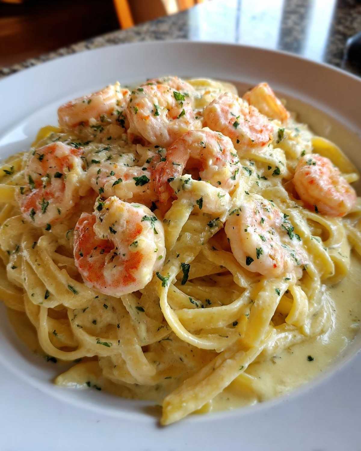 A close-up of fettuccine pasta coated in a rich, creamy sauce, topped generously with pink shrimp and chopped parsley in Creamy Alfredo Shrimp Pasta with Garlic.