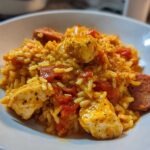 Close-up of a bowl filled with Creamy Cajun Chicken and Rice Skillet featuring chicken pieces, sausage slices, and tomatoes.