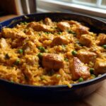 Close-up of Creamy Cajun Chicken Skillet with Rice, featuring seared chicken chunks and green peas in a rich sauce within a blue skillet.