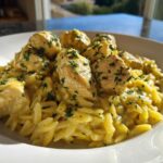 A close-up of a white bowl filled with Creamy Lemon Chicken Orzo with Fresh Herbs, topped with chunks of chicken.