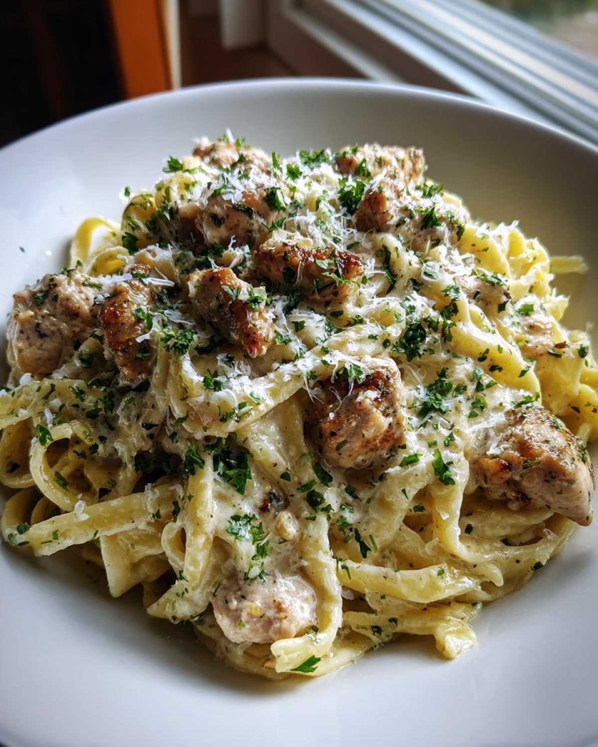 Close-up of a bowl of Creamy Lemon Garlic Pasta with Chicken, topped with parsley and Parmesan.