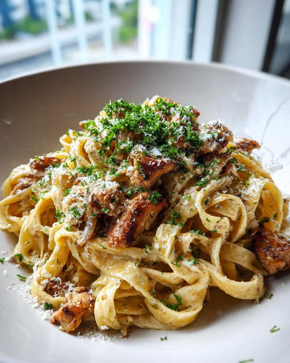 Close-up of creamy lemon garlic pasta with chicken pieces, topped with fresh parsley and grated cheese.