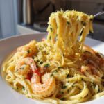 A fork twirls linguine from a bowl of Creamy Lemon Shrimp Pasta with Garlic Sauce, topped with shrimp and lemon zest.