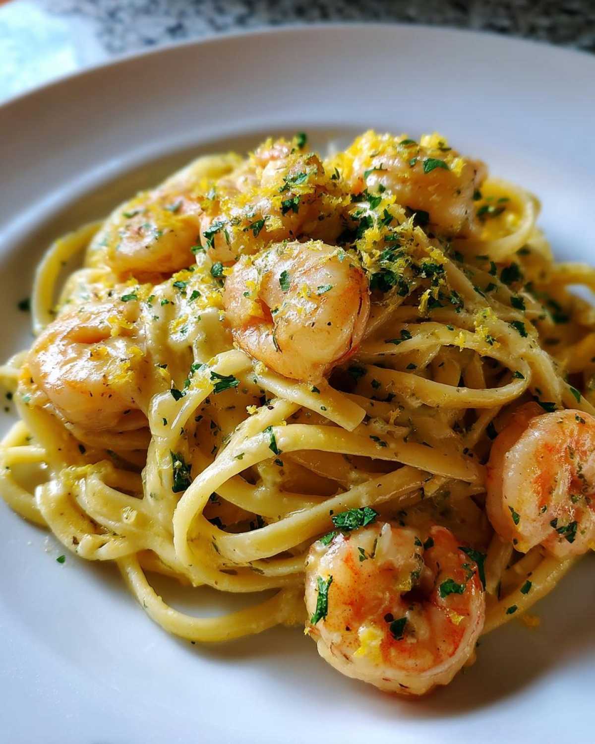 A close-up of a serving of Creamy Lemon Shrimp Pasta with Garlic Sauce, topped with shrimp, zest, and parsley.