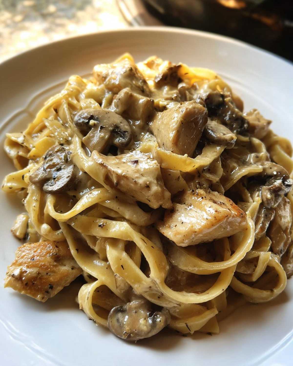 Close-up of rich Creamy Mushroom Chicken Alfredo Pasta featuring fettuccine noodles, chunks of chicken, and sliced mushrooms.