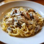 Close-up of fettuccine pasta topped with chicken pieces, sliced mushrooms, and rich sauce in Creamy Mushroom Chicken Alfredo Pasta.