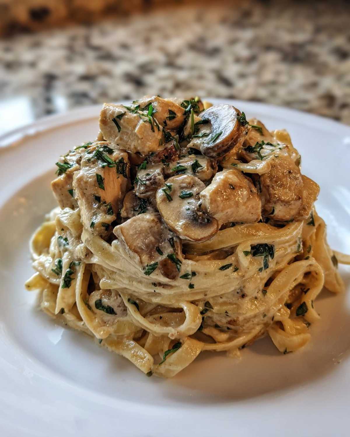 A close-up of a serving of Creamy Mushroom Chicken Alfredo Pasta featuring fettuccine coated in sauce, topped with chicken pieces and sliced mushrooms.
