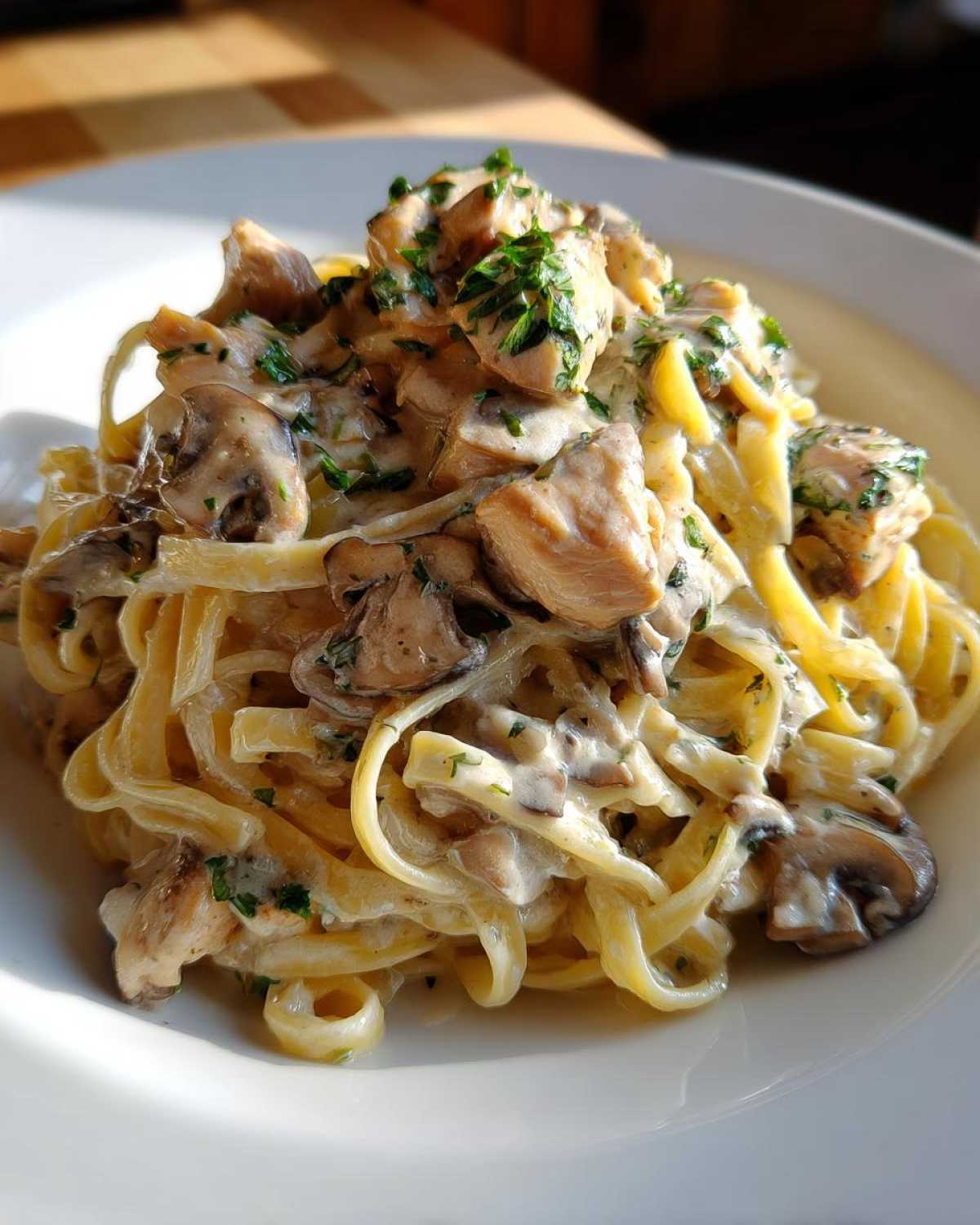Close-up of a white plate piled high with Creamy Mushroom Chicken Alfredo Pasta, garnished with parsley.