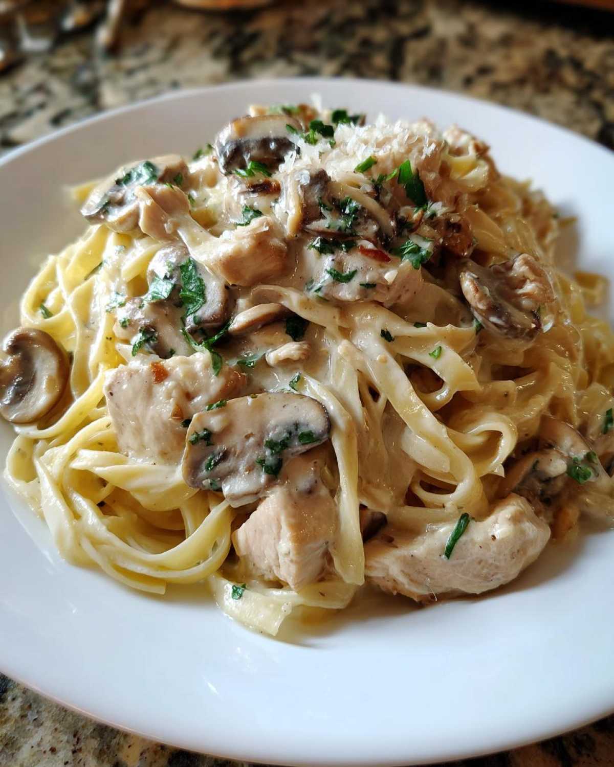 A close-up serving of Creamy Mushroom Chicken Alfredo Pasta featuring fettuccine, sliced mushrooms, chicken pieces, and a sprinkle of Parmesan.